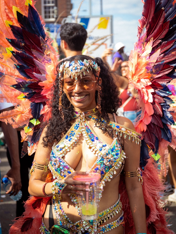 A Woman In A Detailed Blue And Gold Carnival Costume With Large Red And Purple Feathers Smiling For The Camera.
